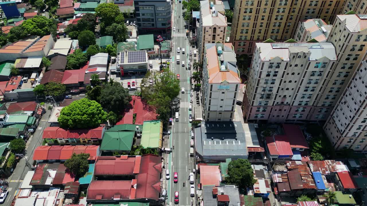 Aerial flyover of a bustling street along residential houses and condominium buildings at West Crame, San Juan City, Philippines during daytime.