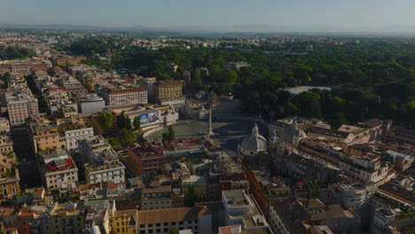 Aerial-slide-and-pan-footage-of-Piazza-del-Popolo,-oval-square-with-obelisk-in-middle-and-historic-north-gate-to-city.-Rome,-Italy