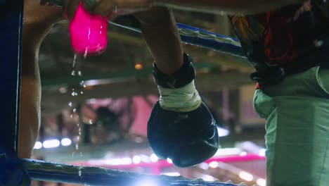 4K-Cinematic-slow-motion-footage-of-a-boxing-glove-from-a-Thai-fighter-arm-hanging-from-the-rope-during-a-Muay-Thai-boxing-fight-with-the-coach-pouring-water-on-the-man