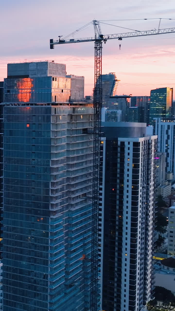 Construction of a skyscraper in Miami. High tower construction crane in the rays of the evening sun. Vertical video. Aerial view