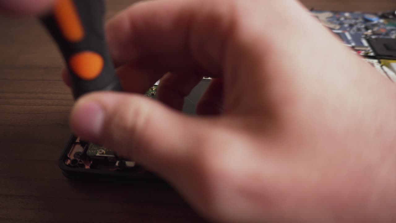 Uomo svita e rimuove un'unità da un laptop usando le mani e un cacciavite.