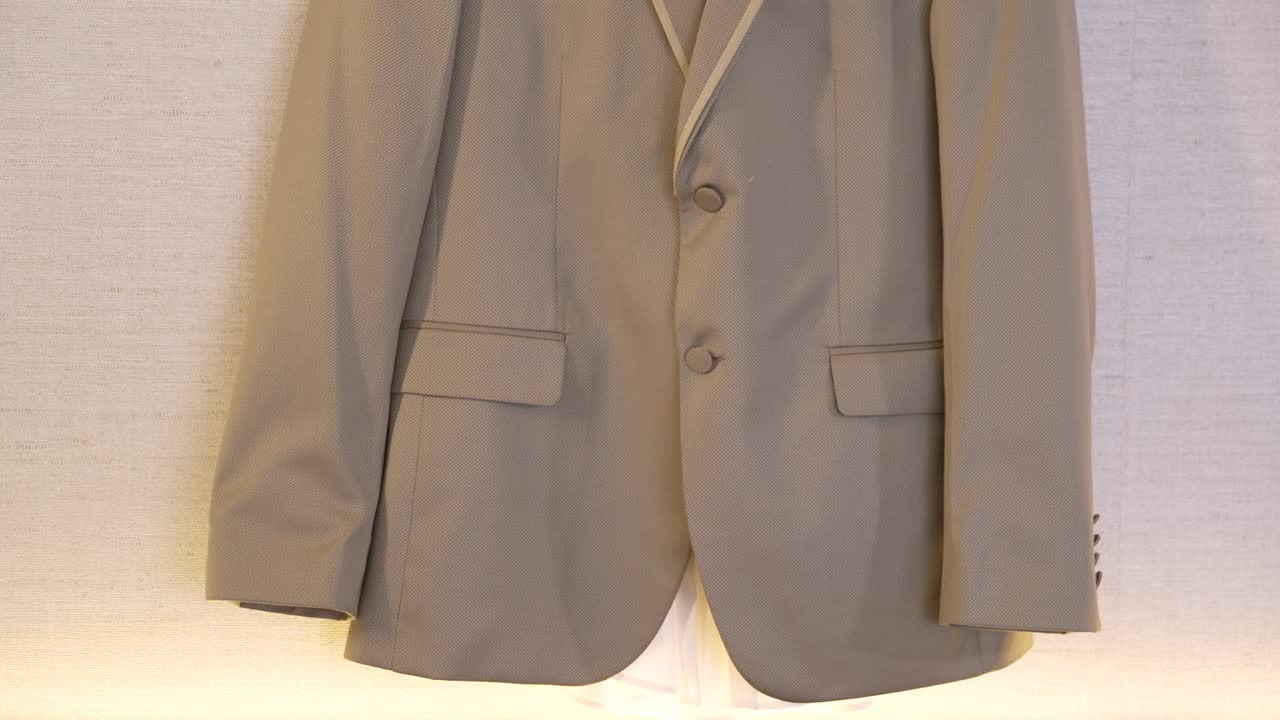Un traje cuelga de una pared en un espacio bien iluminado. El traje es de color claro y tiene un diseño sencillo. Se exhibe de forma ordenada para los compradores en una tienda de ropa o sastrería.