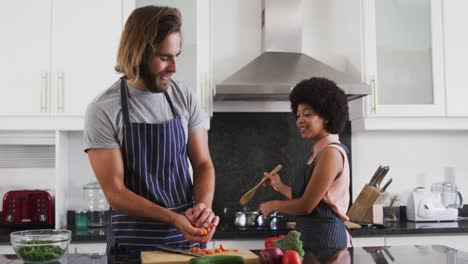 Una-Pareja-De-Raza-Mixta-Usando-Delantales-Cocinando-Comida-Juntos-En-La-Cocina.