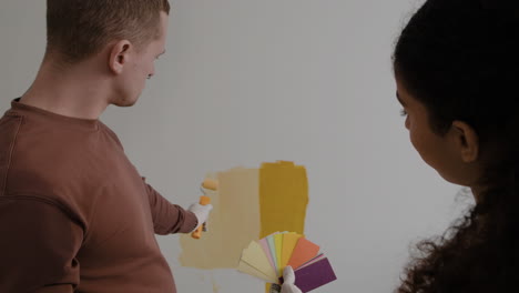 couple painting a wall and choosing paint colors