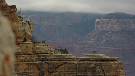 A-pan-starting-behind-a-large-boulder,-revealing-the-South-Rim-of-the-Grand-Canyon,-Arizona