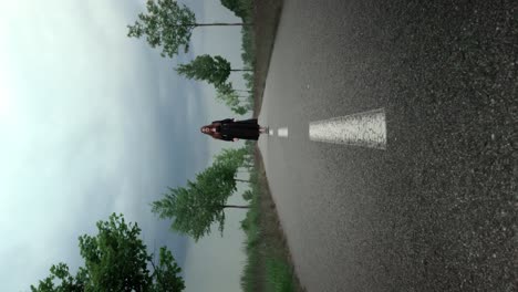 chica en un vestido largo negro se encuentra en el camino de la avenida de los árboles