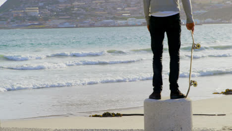 rear view of young caucasian skateboarder standing on the beach and looking at sea 4k