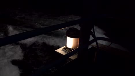 vista lateral de cerca de la luz de seguridad amarilla que brilla en la noche oscura en el ferry mientras las olas del océano blancas y negras pasan