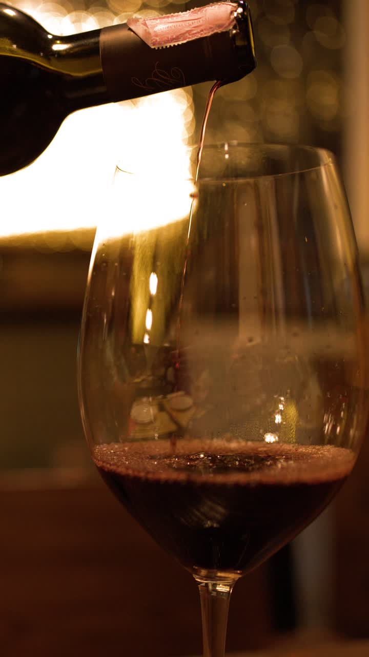 Primo piano di vino rosso versato da una bottiglia in un bicchiere, con luce calda