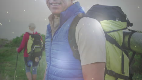 happy caucasian senior couple hiking in countryside, man smiling to camera, over falling light spots