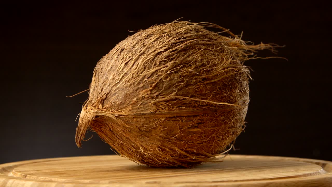coco tropical maduro girando en una mesa de madera contra un fondo negro. frutas tropicales, en bucle