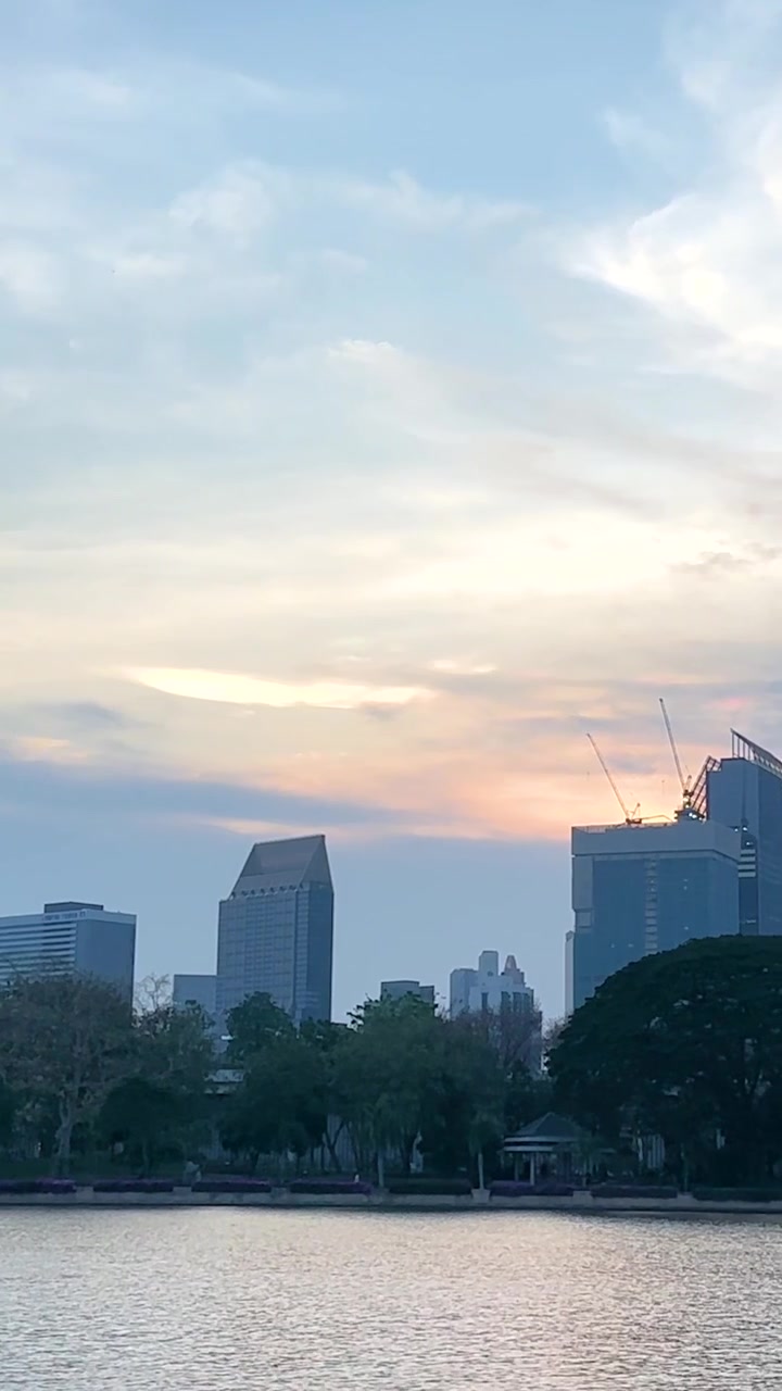 Uma vista serena do pôr do sol sobre o Parque Benjakitti em Bangkok, capturando o horizonte e um lago tranquilo com cores vibrantes.