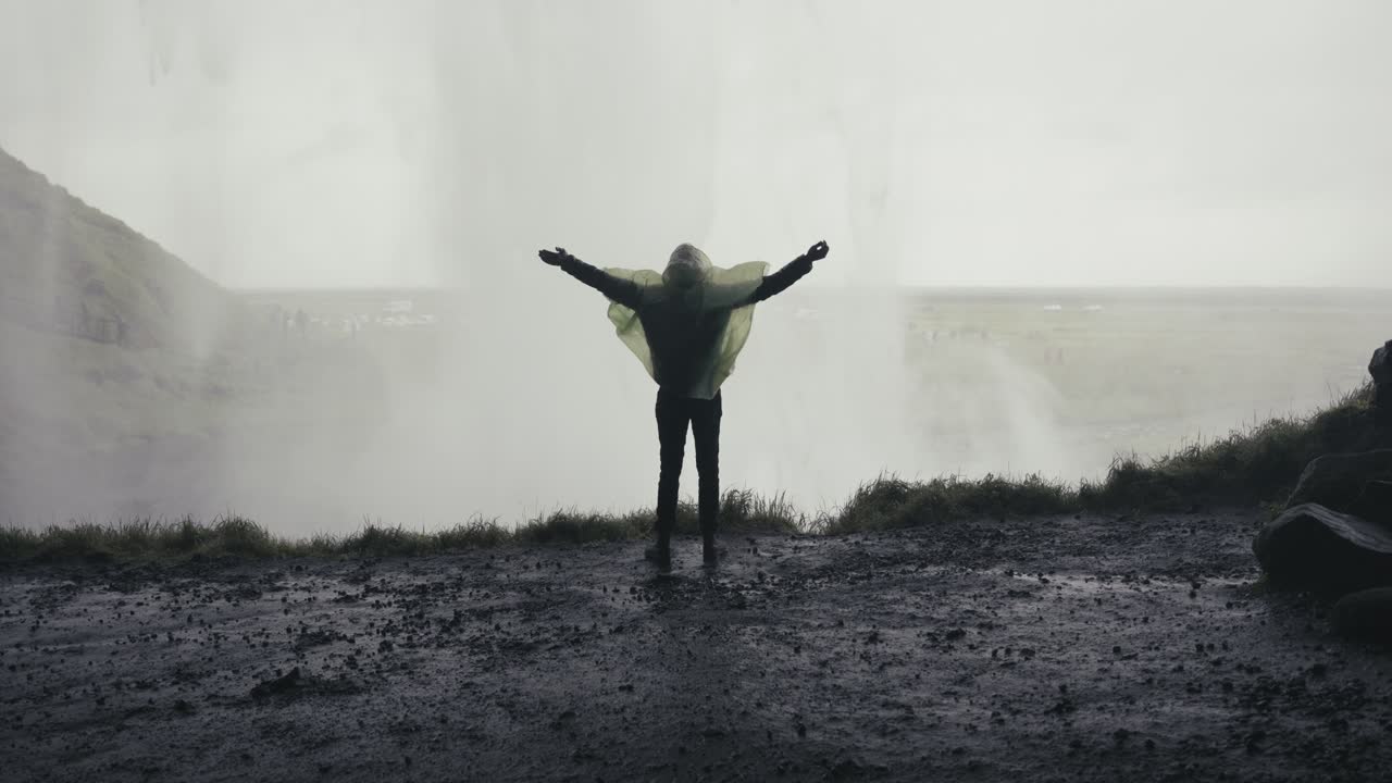 un excursionista solitario camina en cámara lenta hacia una cascada dentro de una cueva