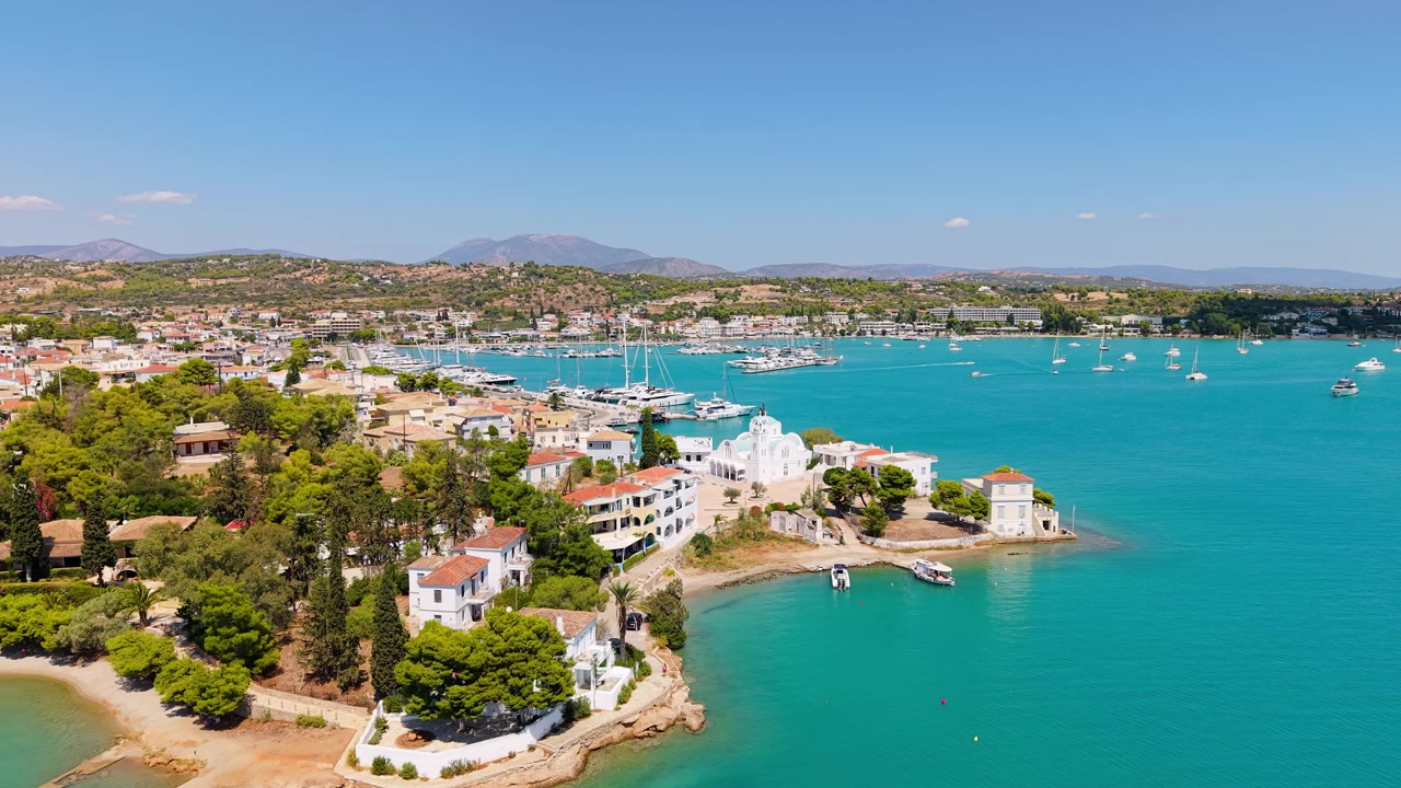 Un drone rivela l'intera penisola di Porto Cheli in estate. Chiesa, ville, marina e baia turchese brillano sotto un cielo limpido con montagne che si estendono fino all'orizzonte.