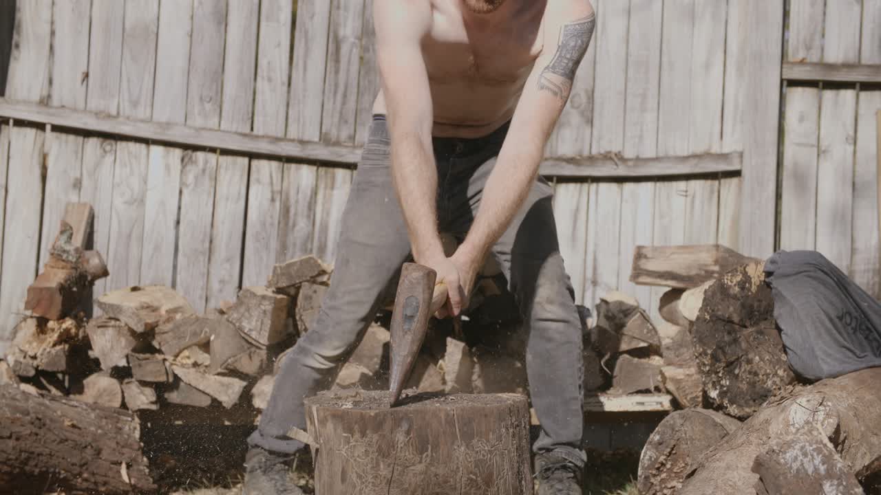 통나무를 쪼개는 셔츠 없는 남자의 슬로우 모션 영상을 닫습니다.