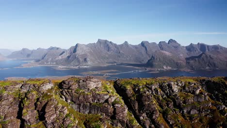 órbita-Aérea-De-Un-Acantilado-Cerca-De-La-Playa-De-Kvalvika-Con-Hermosas-Montañas-Y-Un-Cielo-Azul-Claro-En-El-Fondo,-Islas-Lofoten,-Noruega