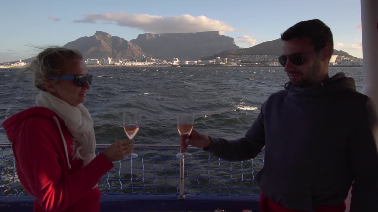 Young People toast glasses of Champagne on the boat overlooking Cape Town and Table Mountain, in Slow Motion