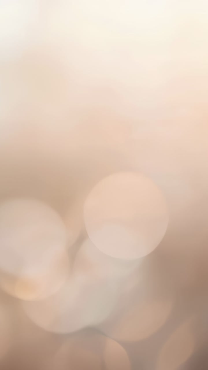 Video verticale: Fotogrammi in movimento che mostrano cerchi bokeh che si spostano e pulsano in un caldo bagliore rosa-beige