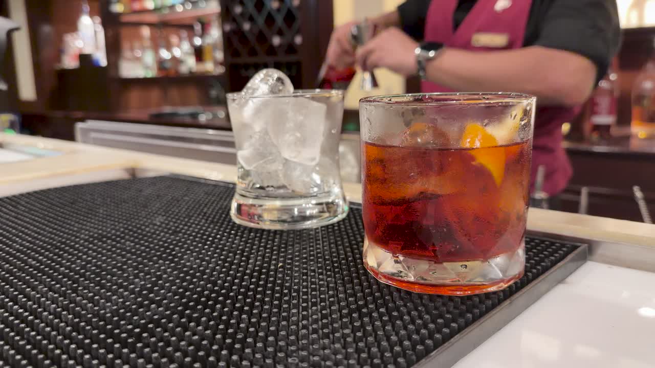 Bartender stirs and serves cocktails in lowball glasses at a warmly lit upscale bar