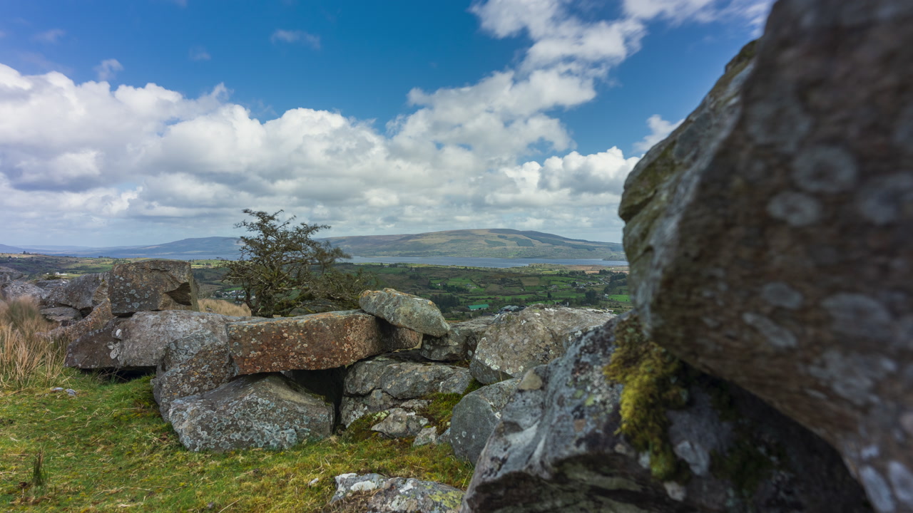 Time lapse of rural landscape with leafless tree in rocky foreground hillside and lake in the distance during a spring sunny cloudy day in Arigna mountains in county Leitrim in Ireland.