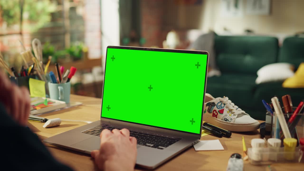 Male Specialist Working on Desktop Computer with Green Screen Mock Up Display at Loft Modern Place. Teenage Freelancer Using his Laptop. Close Up Over the Shoulder
