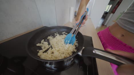 person cooking food in a frying pan in a kitchen