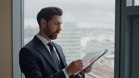 Auditor-checking-financial-documents-standing-smiling-at-office-window-close-up.