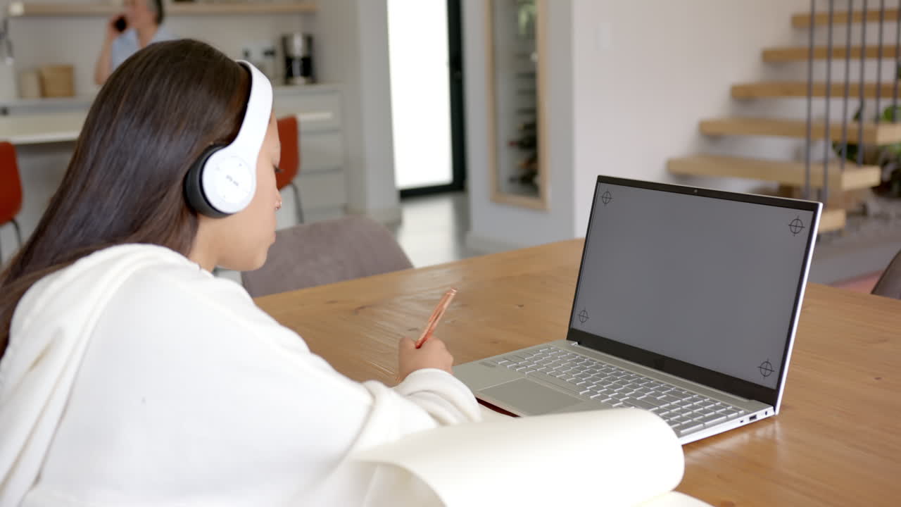 Wearing headphones, girl using laptop and holding smartphone at home desk, copy space