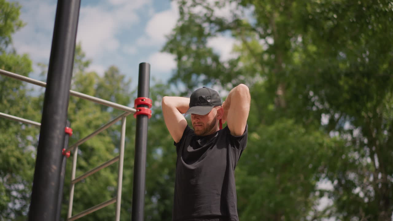 Man exercises outdoors, Male stretches in park surroundings, Person performs calisthenics in leafy open space, Male individual engages in physical warmup routines beneath natural tree canopy