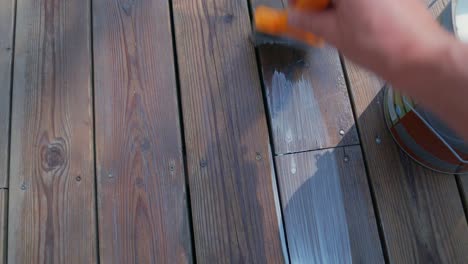 male hand use paint brush to apply wooden oil to the decking