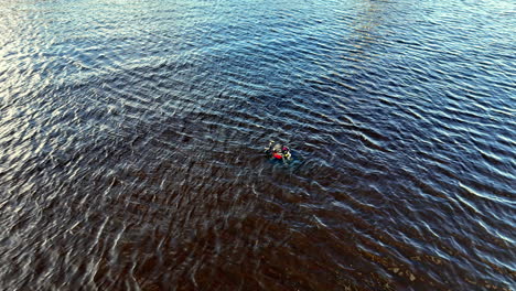 a surface diver swims across rippled open water while towing a bright marker float, captured in a wide aerial frame that emphasizes distance, situational awareness, and calm endurance