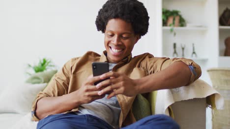 Glücklicher-Afroamerikanischer-Mann,-Der-Zu-Hause-Sein-Smartphone-Nutzt