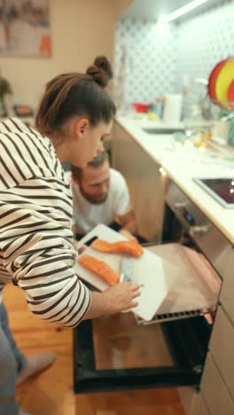 una pareja cocinando salmón en la cocina.
