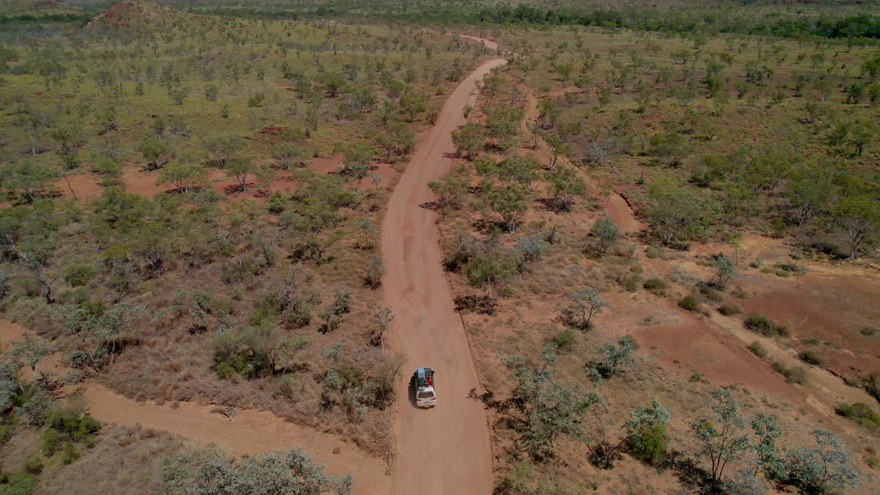Ripresa aerea da drone che segue un veicolo 4x4 che percorre una strada sterrata remota, lasciando i Bungle Bungles nel Parco Nazionale di Purnululu, Australia Occidentale. Paesaggio aspro dell'outback, viaggio avventura e remoto.