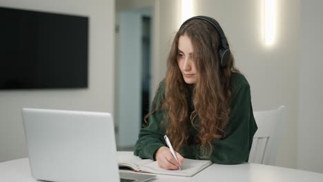 concentrated student girl has distant lesson on laptop, making notes