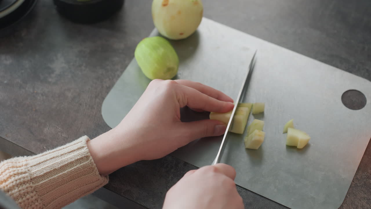 Mujer embarazada cortando una pera en cubos, primer plano de la técnica del cuchillo y agarre firme, manga de suéter y tabla limpia, pequeñas porciones para una comida o puré de bebé, preparación tranquila y organizada para la nutrición prenatal