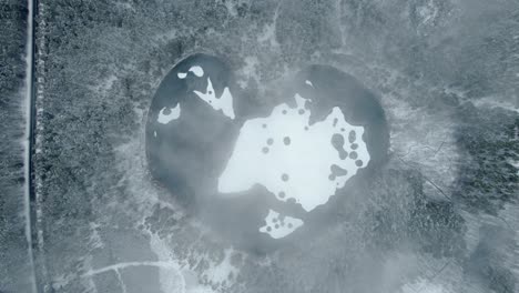 lago congelado en forma de corazón en un bosque nevado desde arriba hacia abajo toma aérea cinematográfica descendente