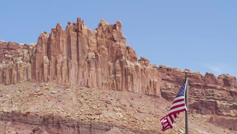 Toma-En-Cámara-Lenta-De-La-Bandera-De-Estados-Unidos-Que-Sopla-En-El-Viento-Frente-A-Las-Montañas-En-El-Parque-Nacional-Capitol-Reef-En-Utah,-Estados-Unidos