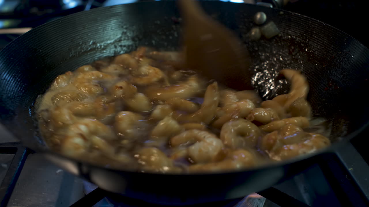 Gamberi mescolati nella salsa all'interno di un wok con un cucchiaio di legno