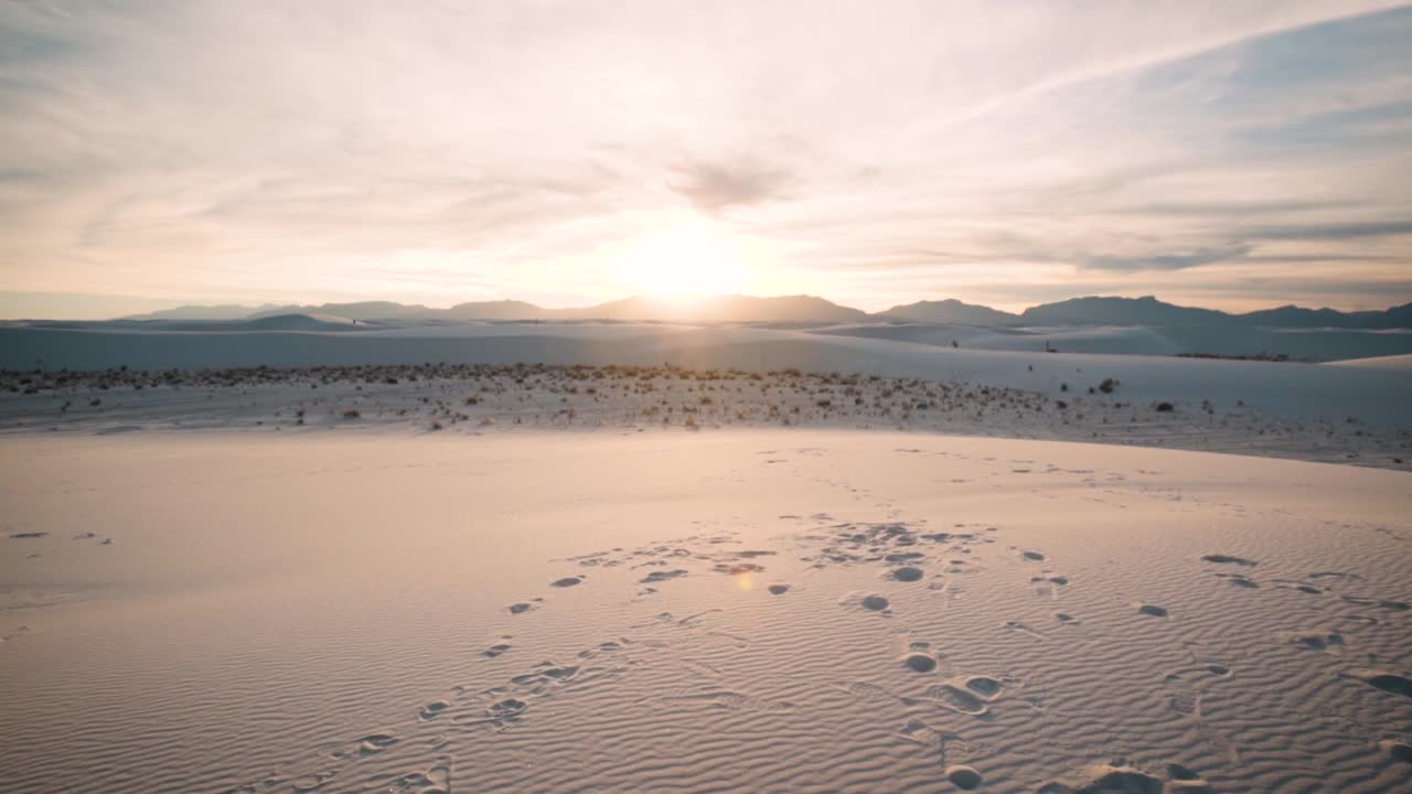 Pan up over footprint covered white sand dunes at sunset