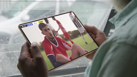 Hombre-Afroamericano-Usando-Una-Tableta-Con-Diversos-Jugadores-De-Fútbol-Masculinos-Jugando-En-La-Pantalla