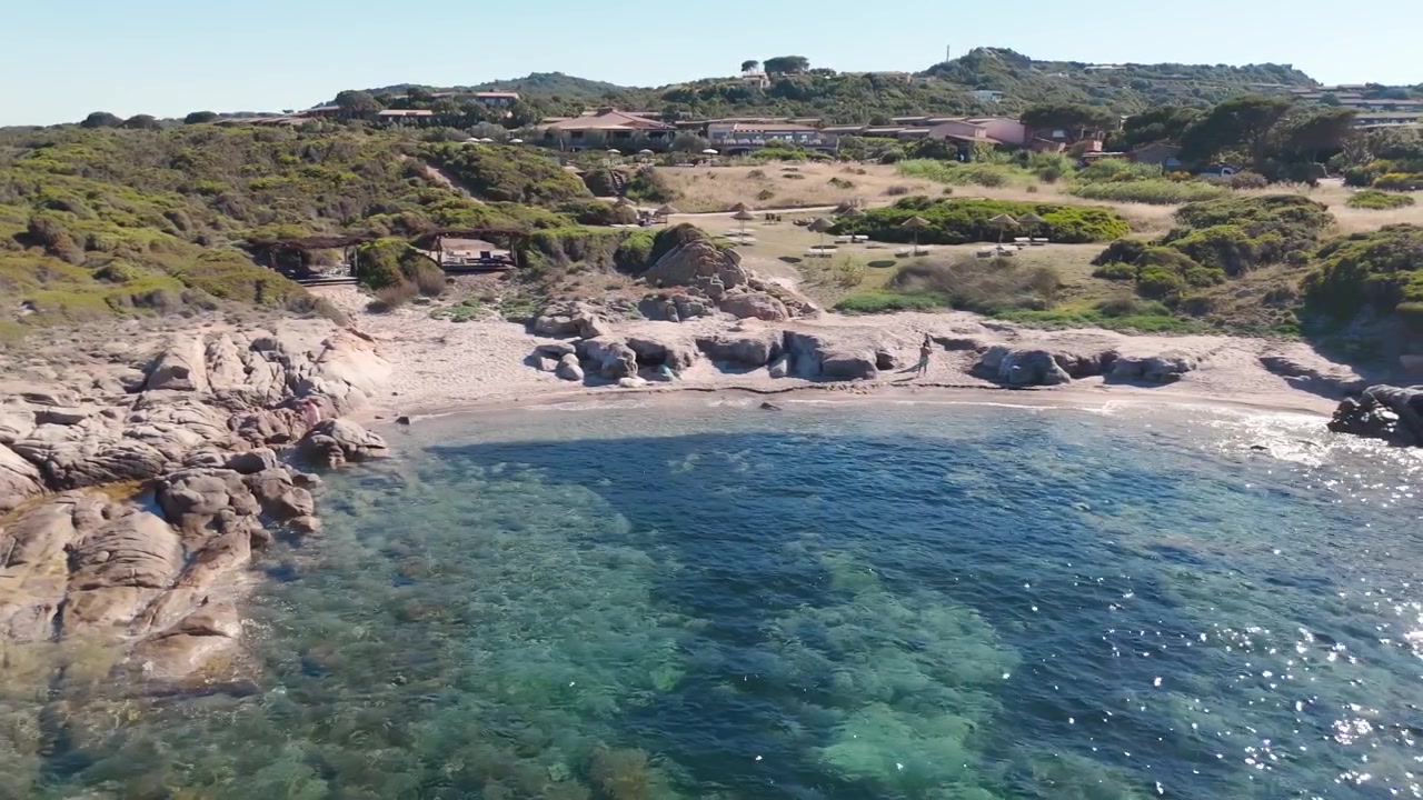 Vista aerea di una costa rocciosa e di un mare blu cristallino vicino a una spiaggia sabbiosa in Sardegna.