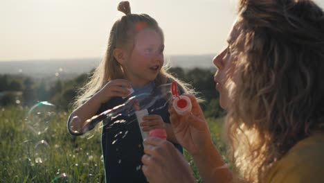 little caucasian girl with mom playing with bubbles at the meadow.