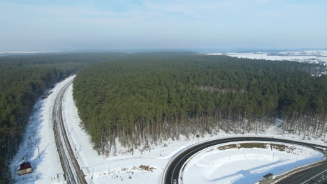 Train-Tracks-And-Curve-Road-Surrounded-By-Green-Forest-During-Winter-Season-In-Rakowice,-Krakow,-Poland