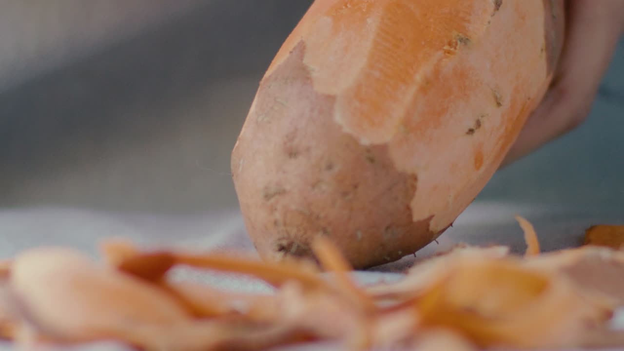 A sweet potato is peeled with a potato peeler, shot in detail and in slow motion