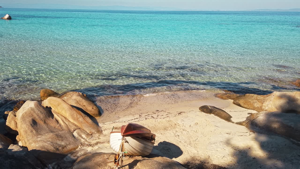 Aegean sea coast with beached boat, rocks on the beach, blue water, Greece. Slow motion