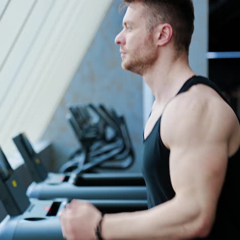 sportsman on a treadmill. athletic man with muscular body training on sports equipment in a gym. fitness guy on a modern simulator. side view. slow motion