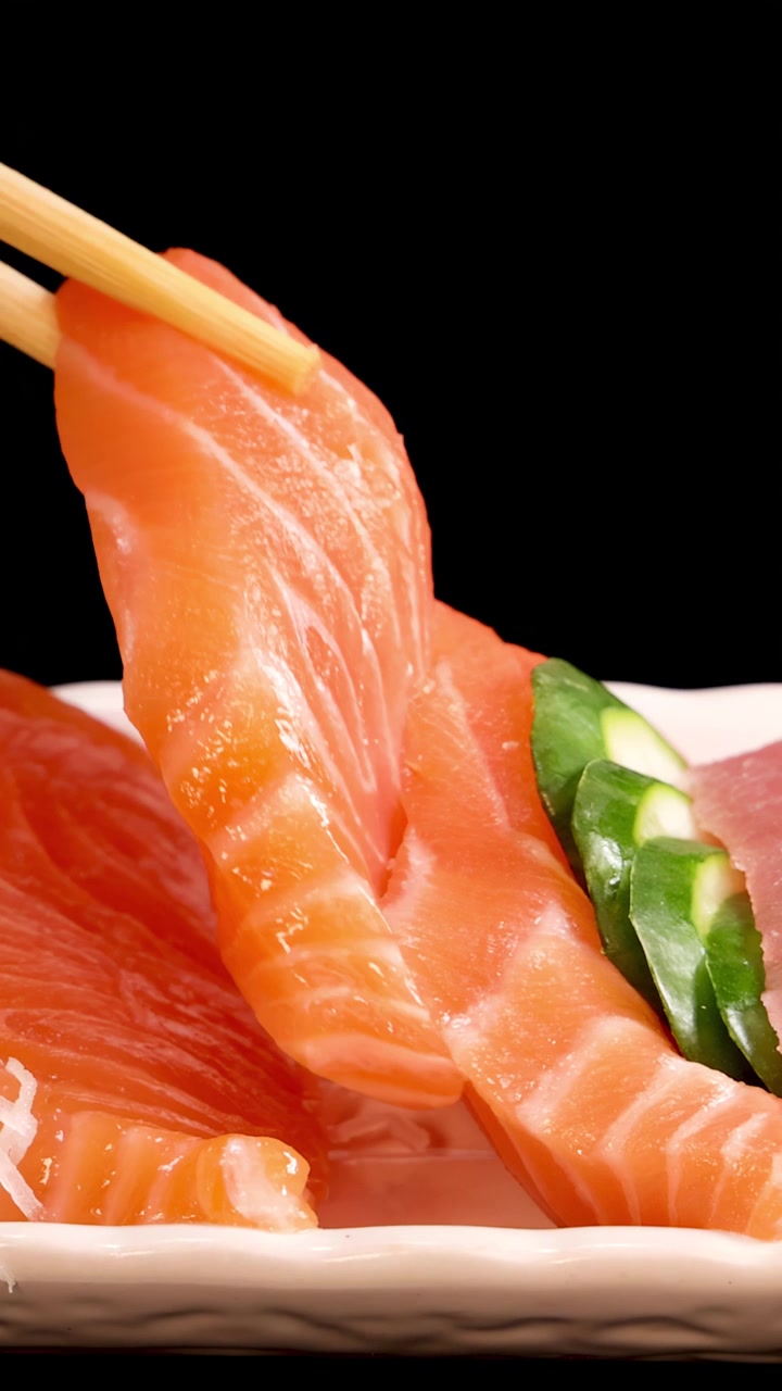 Essstäbchen nehmen Lachs-Sashimi und Jakobsmuschel von einer ansprechend angerichteten Sushi-Platte mit Rogen auf, unter heller Studiobeleuchtung und vor schwarzem Hintergrund.
