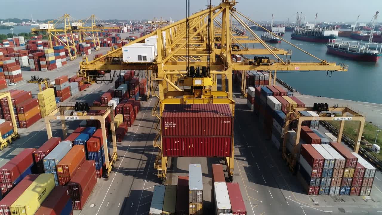 Avvio del sollevamento, carroponte che abbassa e posiziona un container rosso con spreader sul telaio in banchina per il ritiro.