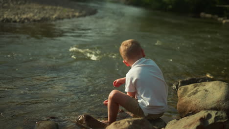 un niño adorable toca el agua con las manos en la orilla del lago. el niño disfruta de un paisaje impresionante con aguas claras de un río de montaña. el concepto de la soledad en el paseo marítimo